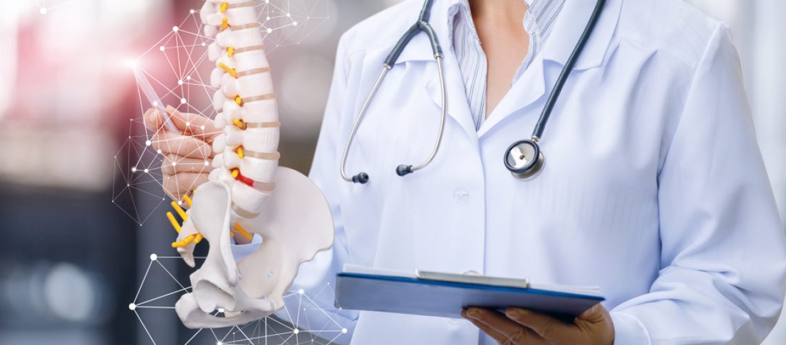 A,Medical,Worker,Shows,The,Spine,On,Blurred,Background.